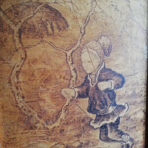 May include: A woodburned image of a child wearing a hat and coat, ice skating on a frozen lake. The child is holding a rope attached to a tree branch, suggesting they are swinging on a rope swing.