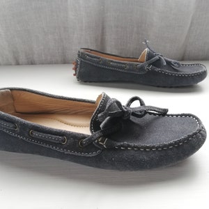 May include: A pair of dark blue suede driving moccasins with a tassel detail and a rubber sole.