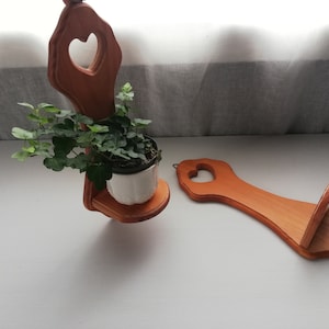 May include: Two wooden wall-mounted plant hangers with heart-shaped cutouts. One hanger has a small potted plant with green leaves.