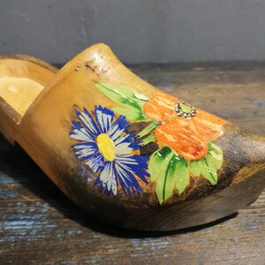 May include: A wooden clog painted with blue, white, yellow, green, and orange flowers. The clog is a traditional Dutch shoe.