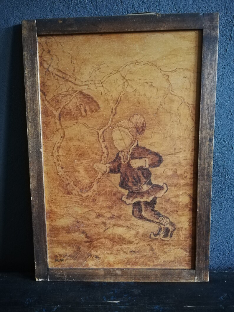 May include: A framed wood-burned artwork depicting a child wearing a hat and coat, standing in a snowy forest scene. The artwork is signed "SUME" in the bottom left corner.