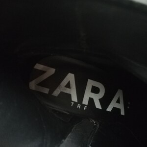 Może przedstawiać: Zbliżenie wnętrza czarnego buta z białym napisem "ZARA TRF" nadrukowanym na wkładce.