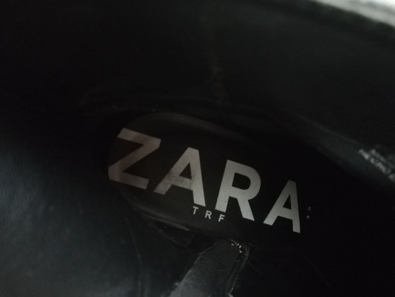 Może przedstawiać: Zbliżenie wnętrza czarnego buta z białym napisem "ZARA TRF" nadrukowanym na wkładce.