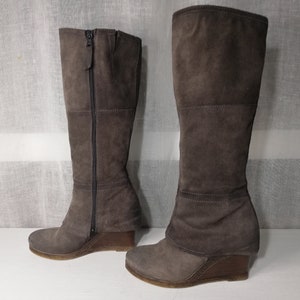 May include: A pair of brown suede wedge boots with a zipper on the back. The boots have a slightly distressed look and a stacked heel.