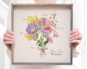May include: A framed print with a watercolor bouquet of flowers. The flowers are labeled with names: Dad, Mom, Grace, Ashley, Christian. The text at the bottom reads "Bless This Bouquet".