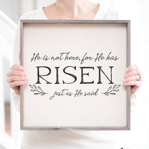May include: A framed canvas sign with the text "He is not here, for He has RISEN just as He said" in black lettering with a small leafy design on either side of the text.