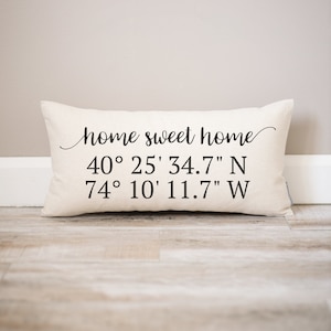 May include: White pillow with black text that reads "home sweet home" and coordinates "40° 25' 34.7" N 74° 10' 11.7" W".