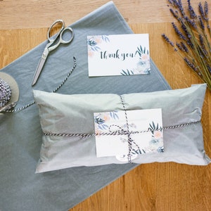 May include: A gift wrapped in white tissue paper with black and white twine. The gift is tied with a floral card and a small tag that says "Thank you".
