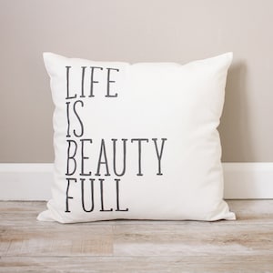 May include: White cushion with black text that reads "Life is Beauty Full".