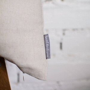 May include: A close-up of a beige fabric pillow with a gray label that reads "Sweet Indulgence".