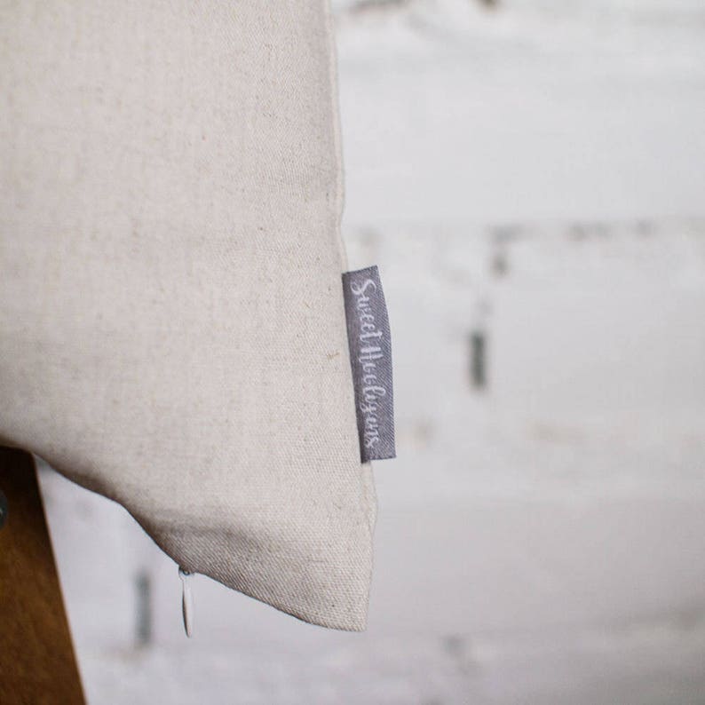 May include: A close-up of a beige fabric pillow with a gray label that reads "Sweet Indulgence".