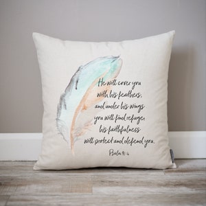 Op de afbeelding: Een beige kussen met een aquarel veren ontwerp en de tekst "He will cover you with his feathers, and under his wings you will find refuge, his faithfulness will protect and defend you. Psalm 91:4"