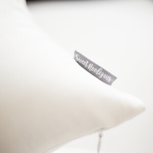 May include: A white pillow with a gray tag that reads "Sweet Hooligans" in cursive. The pillow is a solid white color and appears to be made of a soft material. The tag is attached to the side of the pillow.
