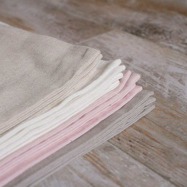 May include: A stack of linen napkins in various shades of pink, white, and beige. The napkins are folded and arranged in a graduated color scheme, with the lightest shade at the top and the darkest shade at the bottom.