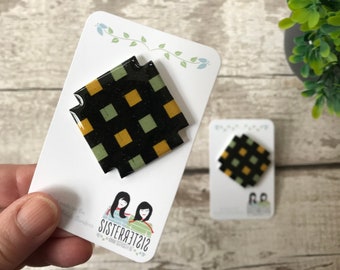 Puede incluir: Dos pines de resina con un patrón de cuadros negros, amarillos y verdes. Los pines están en tarjetas blancas con el texto "Sister312" en una tarjeta.