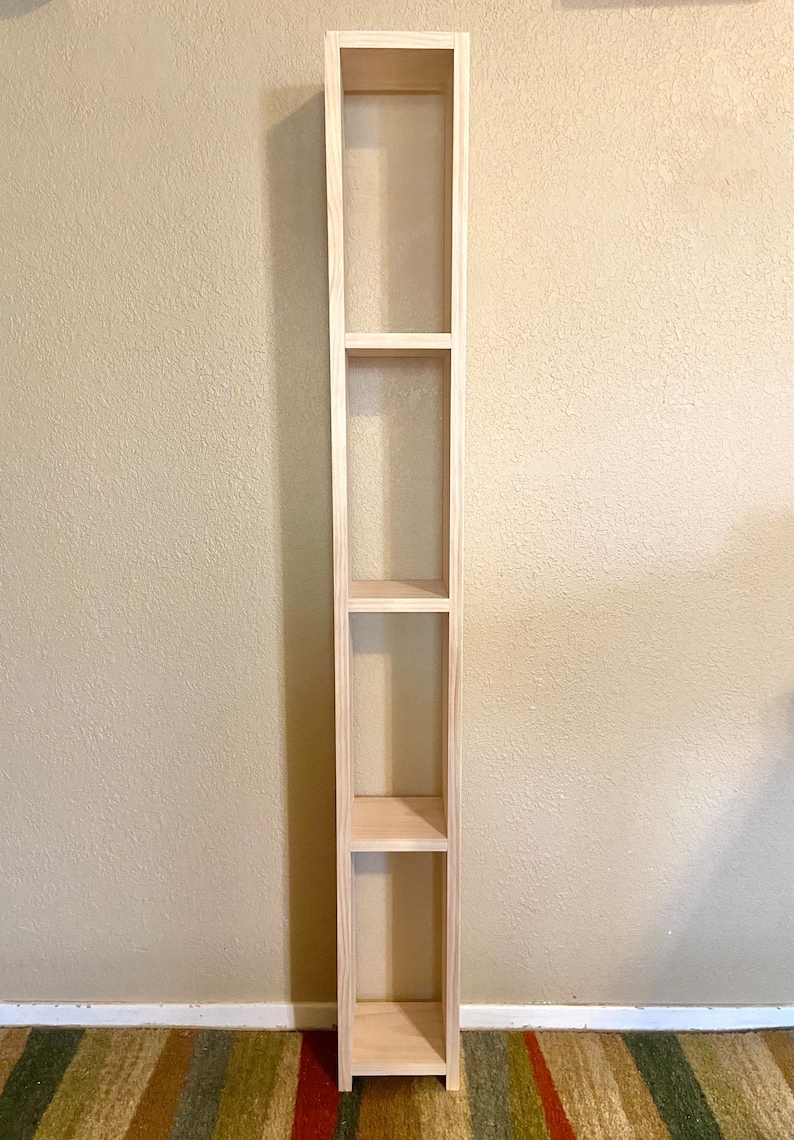 May include: A tall, wooden shelf unit with four open shelves. The shelf is made of light wood and has a simple, modern design.