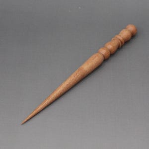 Könnte beinhalten: Ein handgefertigter Haarstab aus hellem Holz mit spitz zulaufendem Ende und dekorativer, abgerundeter Spitze. Das Haaraccessoire dient dazu, das Haar in einer Hochsteckfrisur zu befestigen. Die Gesamtlänge beträgt ca. 15 cm.