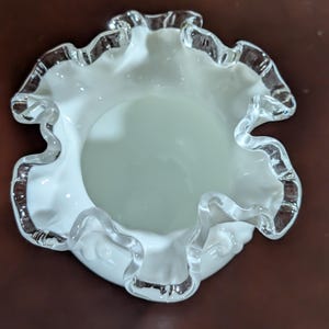 May include: A white glass bowl with a ruffled edge. The bowl has a clear glass rim.