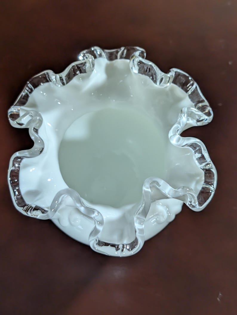 May include: A white glass bowl with a ruffled edge. The bowl has a clear glass rim.