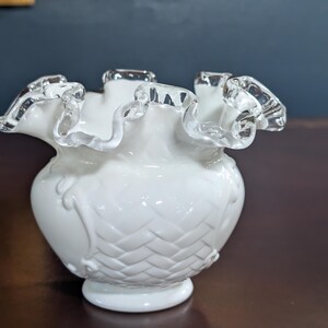 May include: A white milk glass vase with a ruffled top and a woven pattern. The vase has a silver trim around the top.