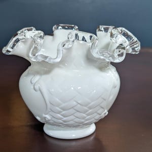 May include: White milk glass vase with a ruffled top and a woven pattern. The vase has a silver trim around the top.