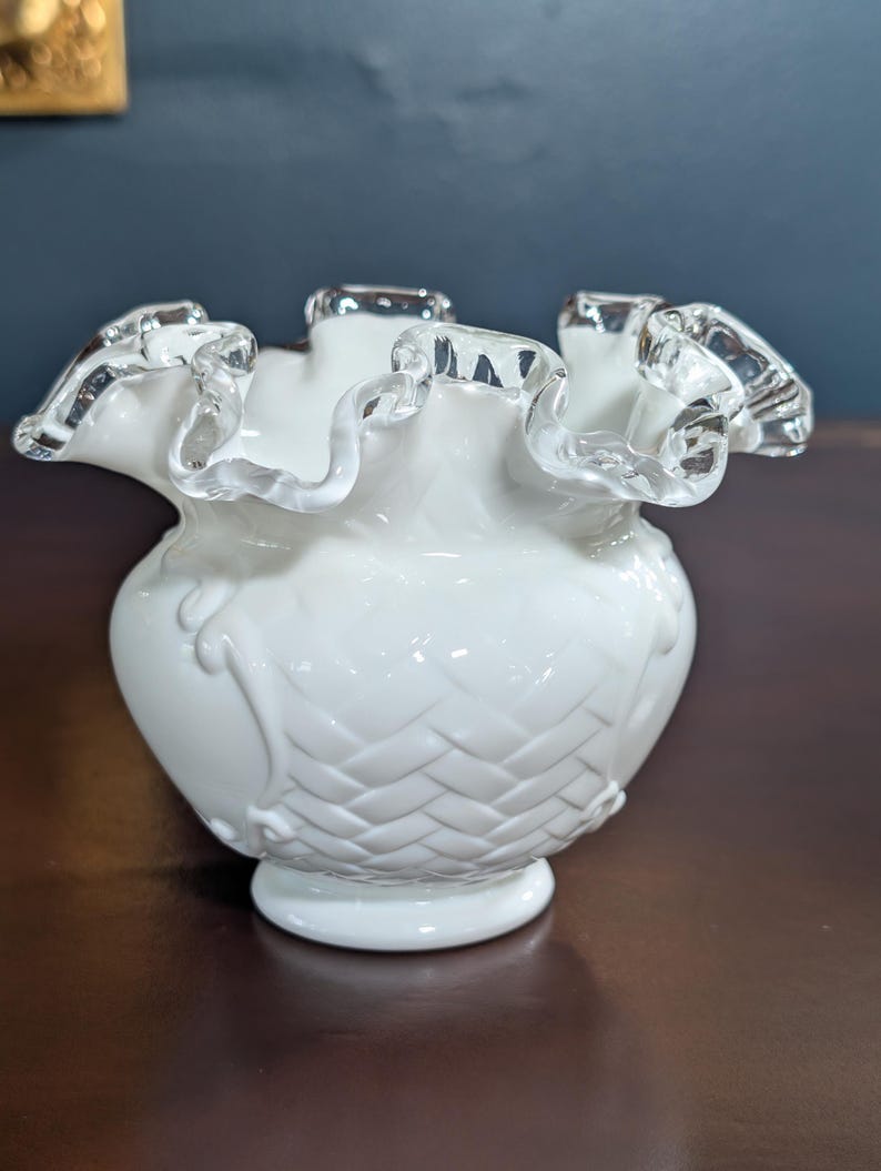 May include: White milk glass vase with a ruffled top and a woven pattern. The vase has a silver trim around the top.
