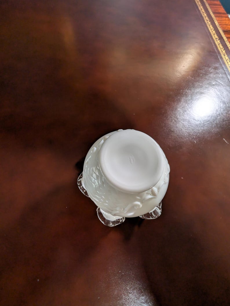 May include: White ceramic bowl with a floral design and a scalloped edge. The bowl is sitting on a brown leather surface.