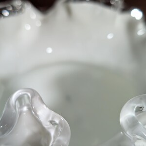 May include: White glass vase with a ruffled rim. The vase is made of clear glass with a frosted finish.