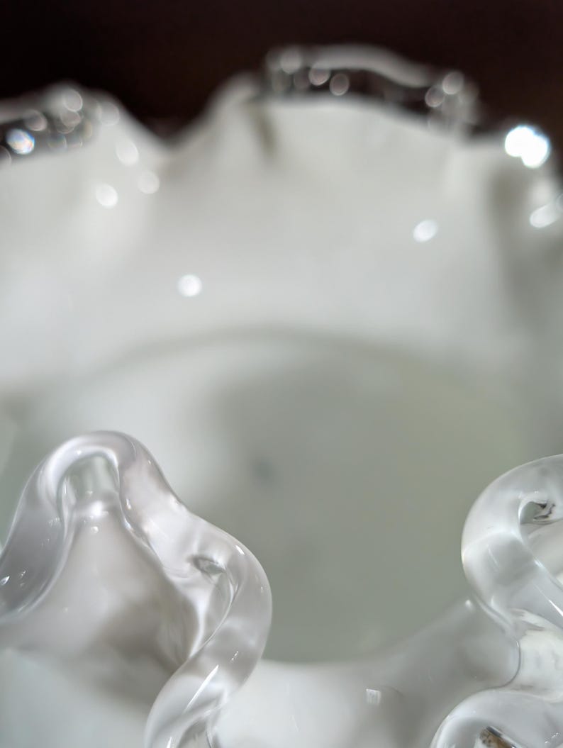 May include: White glass vase with a ruffled rim. The vase is made of clear glass with a frosted finish.