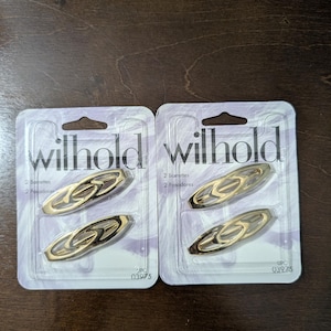 May include: Two packages of hair barrettes. Each package contains two gold-toned oval barrettes. The packaging is white and purple with the word "willhold" printed in a stylized font. The UPC code is 03975.