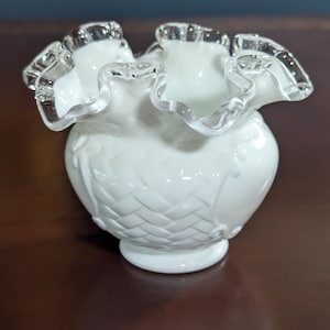 May include: A white ruffled glass vase with a woven pattern and a silver trim around the top.