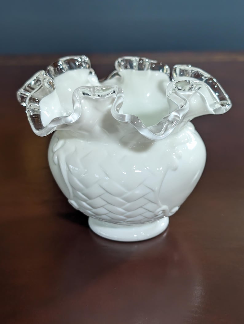May include: A white ruffled glass vase with a woven pattern and a silver trim around the top.