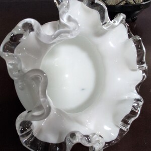 May include: White glass bowl with a ruffled edge. The bowl is made of clear glass with a white interior.