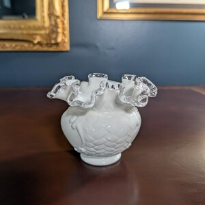 May include: A white glass vase with a ruffled, silver-trimmed rim. The vase has a textured, diamond-shaped pattern and a rounded base.