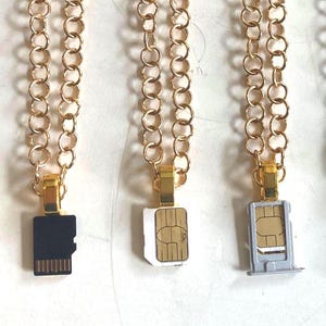以下が含まれることがあります： 再利用された電子部品で作られたユニークなペンダントが特徴のネックレスのコレクション。ペンダントには、CPU、SDカード、SIMカード、回路基板の破片が含まれており、金と銀のチェーンに吊り下げられています。