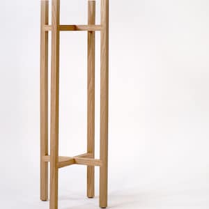 May include: A wooden plant stand with a simple, rectangular design. The stand is made of natural wood and has a light brown finish.