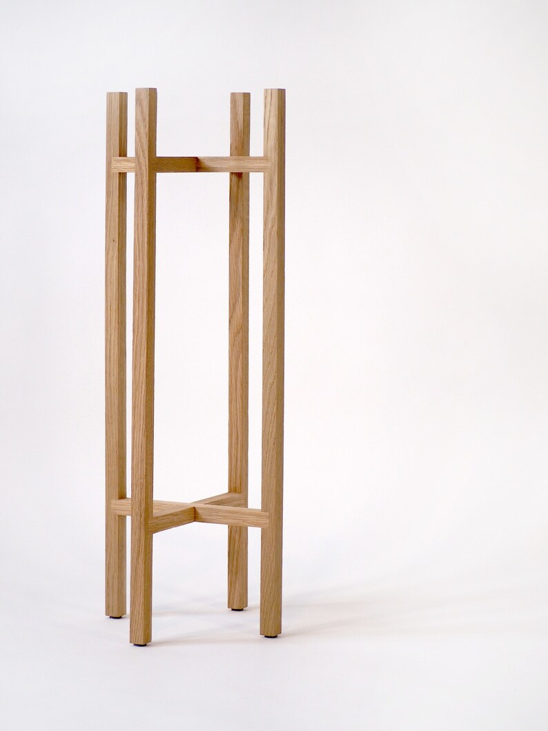 May include: A wooden plant stand with a simple, rectangular design. The stand is made of natural wood and has a light brown finish.