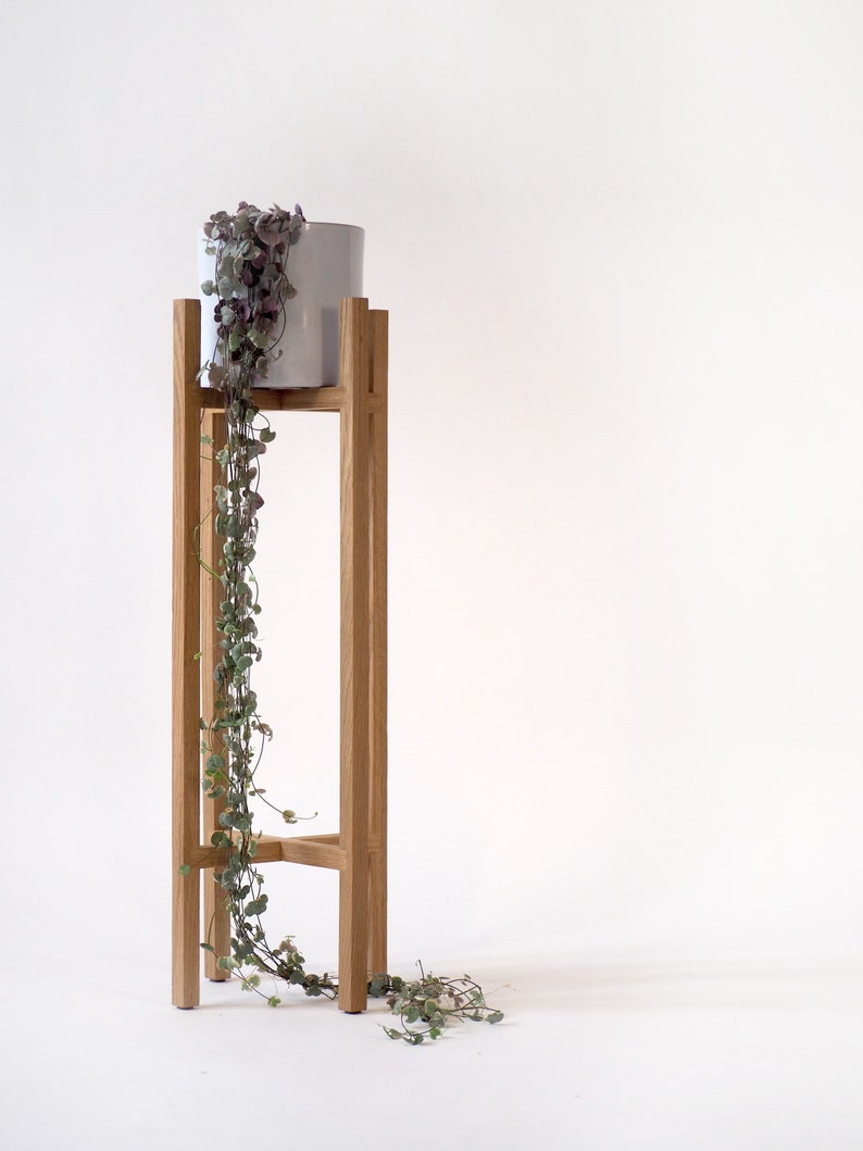 May include: A wooden plant stand with a white ceramic pot and a trailing plant with green leaves and purple flowers.