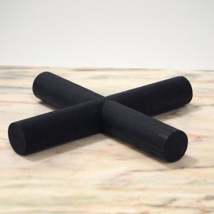 May include: A black wooden coaster in a cross shape. The coaster is made of four cylindrical pieces of wood that intersect in the centre. The coaster is on a light-coloured surface.