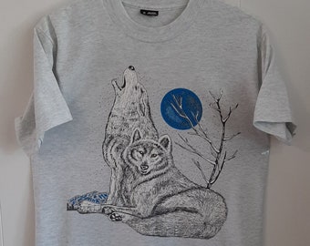 Puede incluir: Una camiseta gris con un gráfico de dos lobos aullando a la luna. La luna es azul y los lobos son blanco y negro.