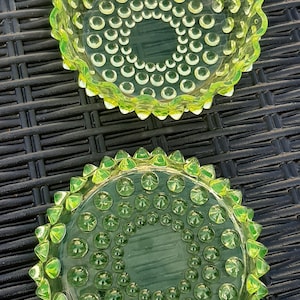 May include: Two green glass ashtrays with a textured, bubbled surface. The ashtray on the top has a scalloped edge. The ashtray on the bottom has a spiky edge.