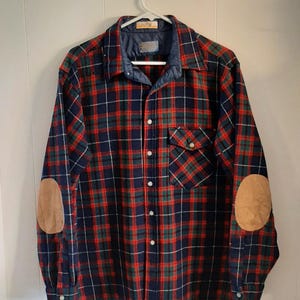 May include: A long-sleeved flannel shirt with a red, green, and blue plaid pattern. The shirt has two suede elbow patches and a single chest pocket.