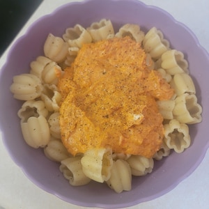 May include: A bowl of pasta with a vibrant orange sauce. The pasta is a unique shape, and the sauce is sprinkled with black pepper. The bowl is a light purple color.