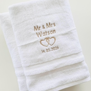 Pu&ograve; includere: Due asciugamani bianchi con ricamo "Mr & Mrs Watson" sopra due cuori intrecciati e la data "14.05.2026". Il ricamo &egrave; di colore marrone chiaro.