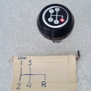 May include: A black shift knob with a white and black gear pattern, including numbers 1, 2, 3, 4, and R for reverse. A diagram of the gear pattern is below the knob.