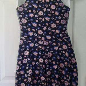 May include: A sleeveless dress with a halter neck, patterned with small pink and blue flowers on a dark navy background. The dress is displayed on a white mannequin. The dress is a summer garment.