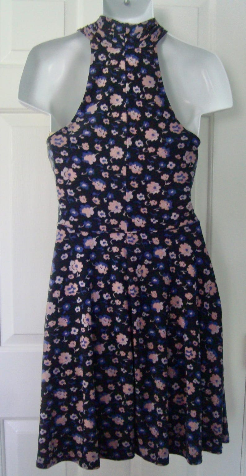 May include: A sleeveless dress with a halter neck, patterned with small pink and blue flowers on a dark navy background. The dress is displayed on a white mannequin. The dress is a summer garment.