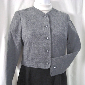 May include: A gray, textured, long-sleeved jacket with a round neckline and a front button closure. The jacket features a subtle speckled pattern throughout the fabric, long sleeves with a single button at each cuff, and a cropped length.