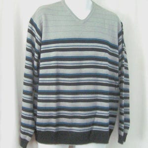 Peut inclure: Un pull à manches longues et col en V présentant un motif à rayures horizontales dans des tons de gris clair, gris anthracite et bleu. La partie supérieure de la poitrine est gris clair uni, tandis que le reste affiche des rayures.