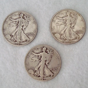 Op de afbeelding: Drie zilveren Walking Liberty halve dollars uit 1943. Elke munt toont een vrouw die naar de zon loopt met de woorden "IN GOD WE TRUST". Het jaartal "1943" is zichtbaar op elke munt.